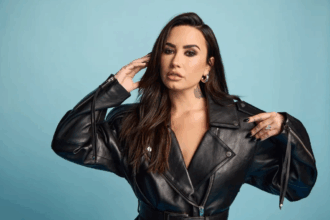 Demi Lovato mengenakan jaket kulit hitam berpose di depan latar biru.